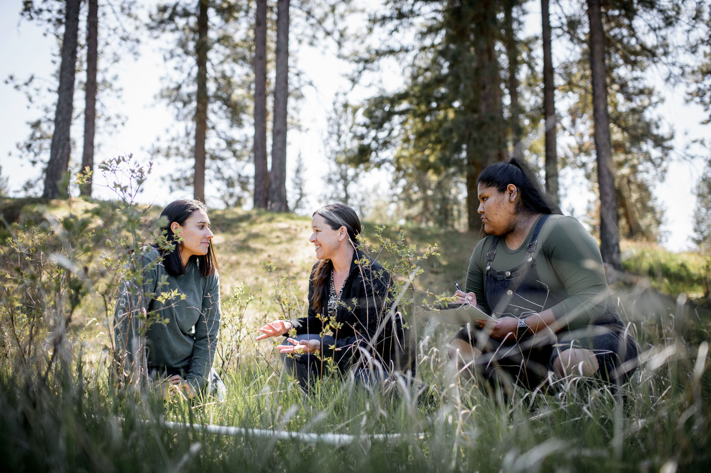 Three females sitting and talking in a forest.