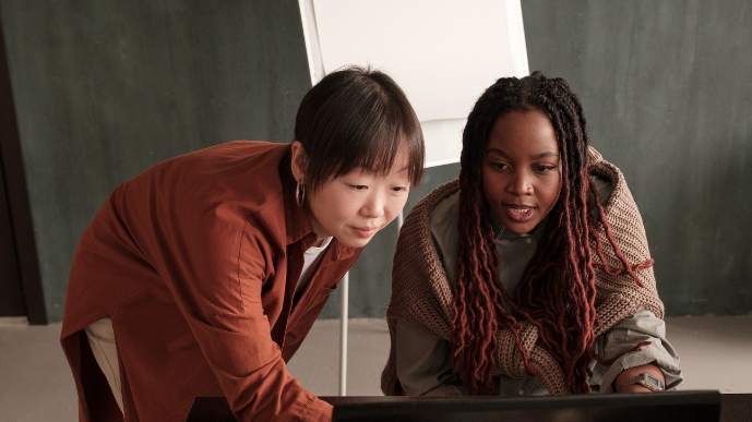 Two women working side by side in front of a computer screen.