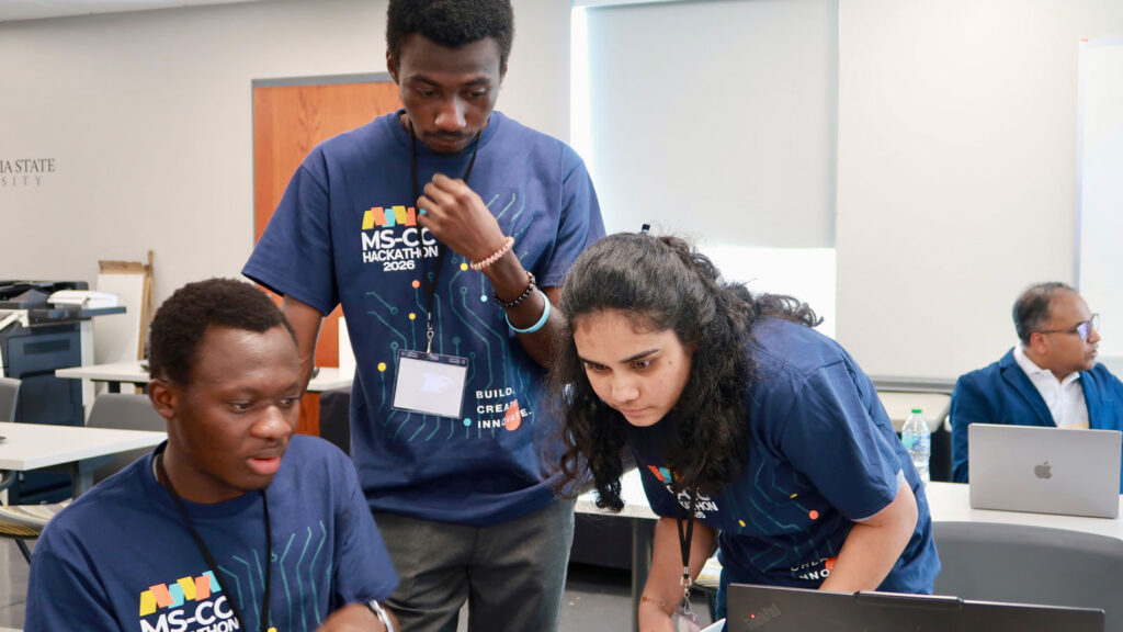 Three MS-CC hackathon students brainstorming in a university classroom.