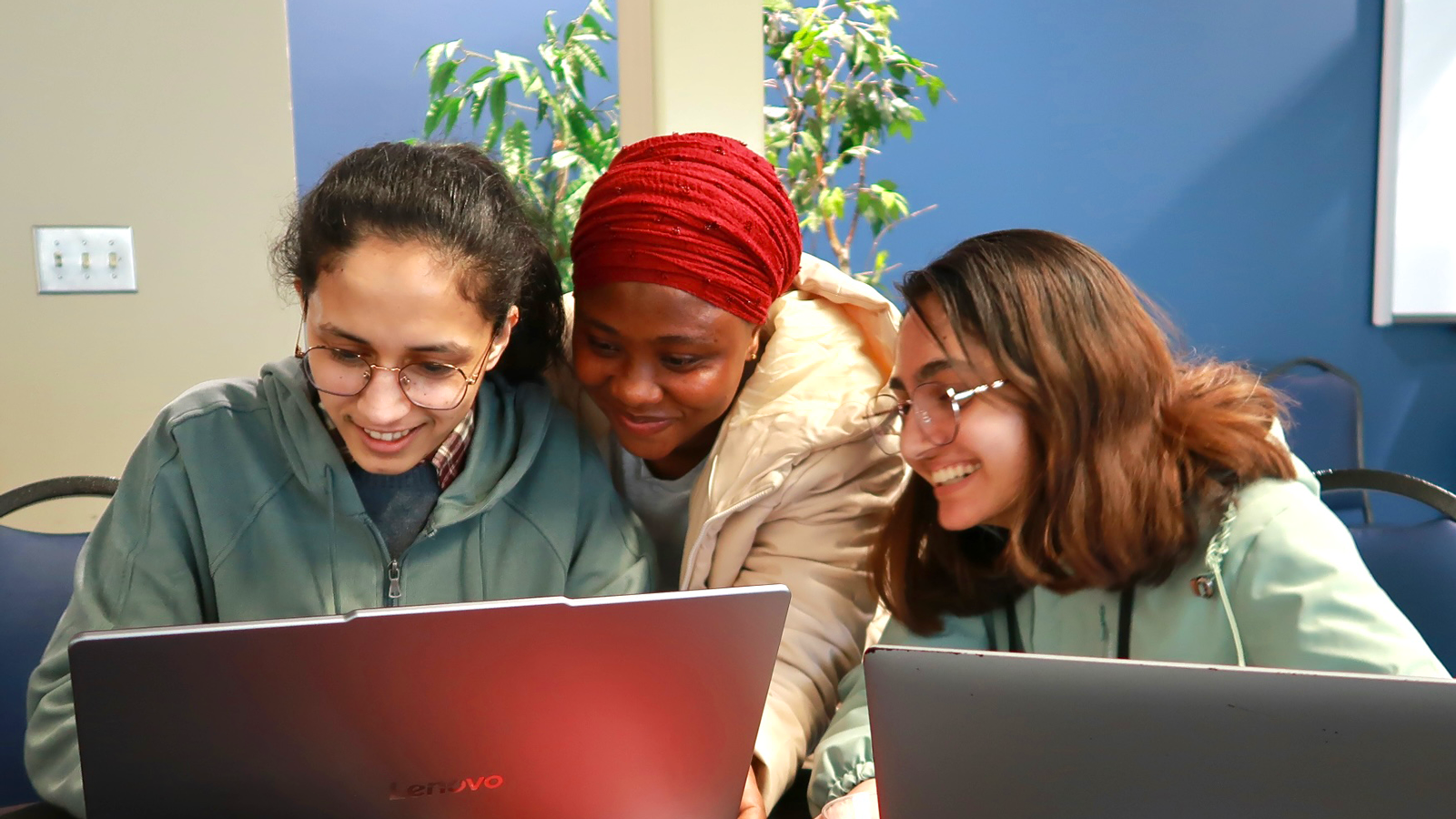 Three female students collaborating over a laptop computer.