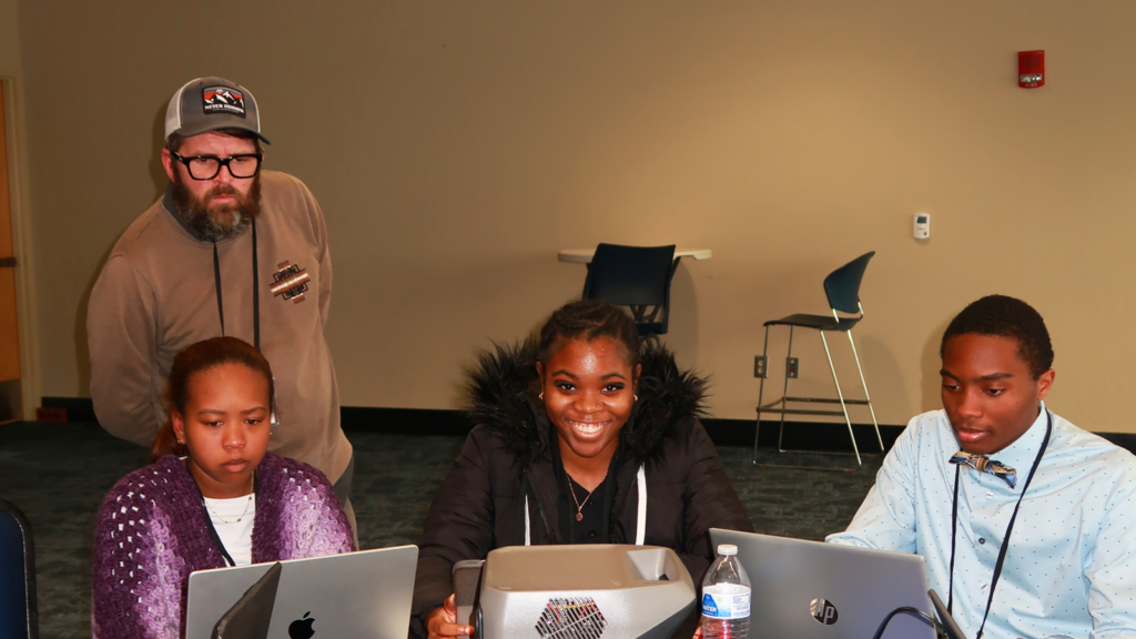 Students sitting around a table with an instructor in the back.