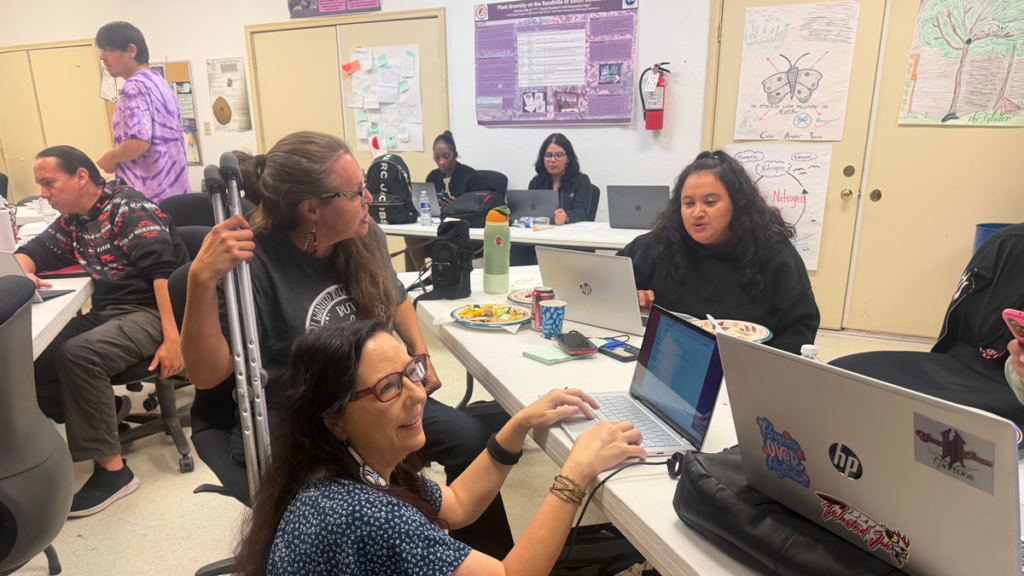 A group of participants collaborating around tables with laptops during the 2026 Oglala Lakota hackathon.